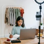 woman sitting on a short table in front of a laptop writing.